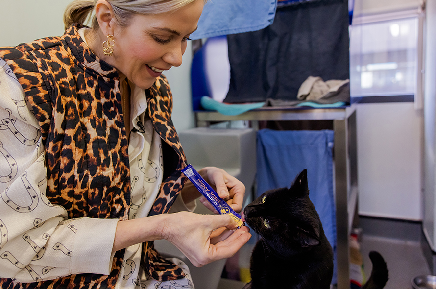 A woman feeding a black cat a treat