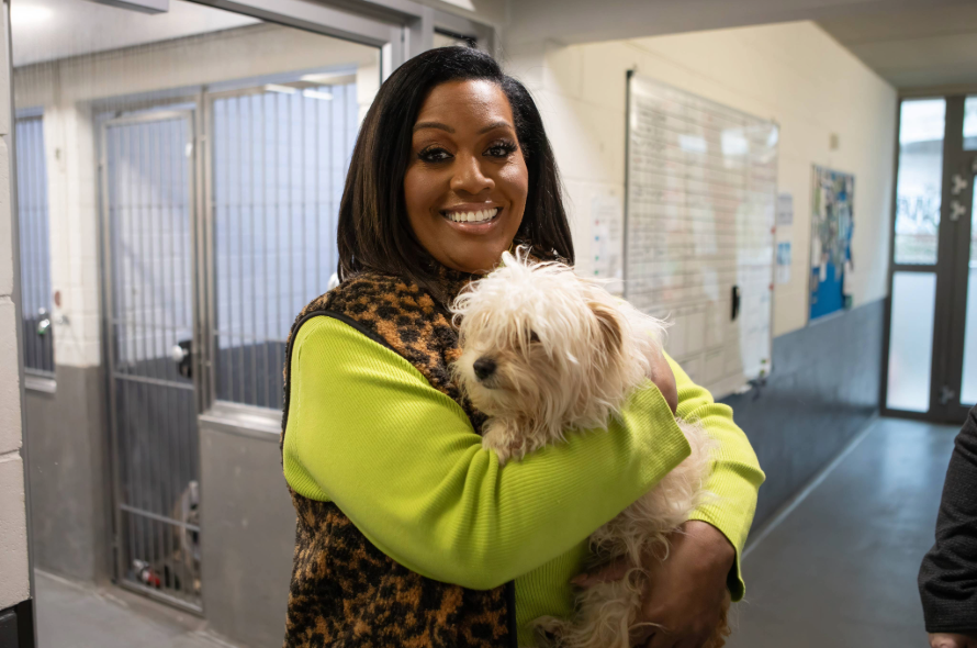 TV presenter holding a scruffy white dog 