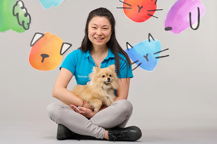 Battersea staff member sitting cross legged holding a Pomeranian 