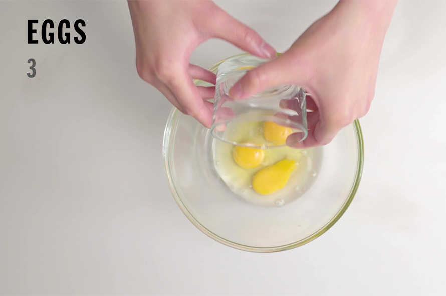 Pouring 3 eggs into a glass bowl