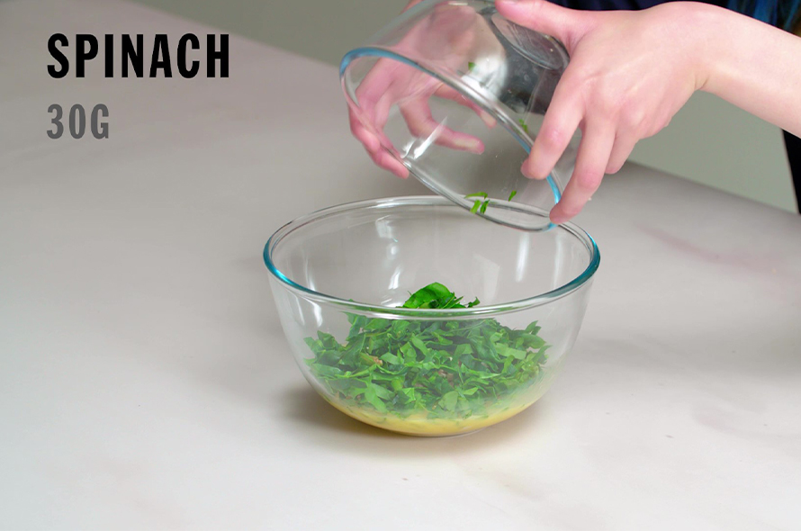 Pouring a bowl of spinage into the chicken and egg mixture