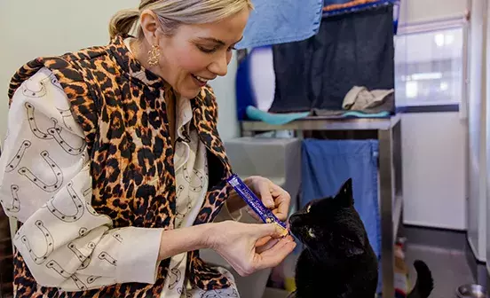 A woman feeding a black cat a treat